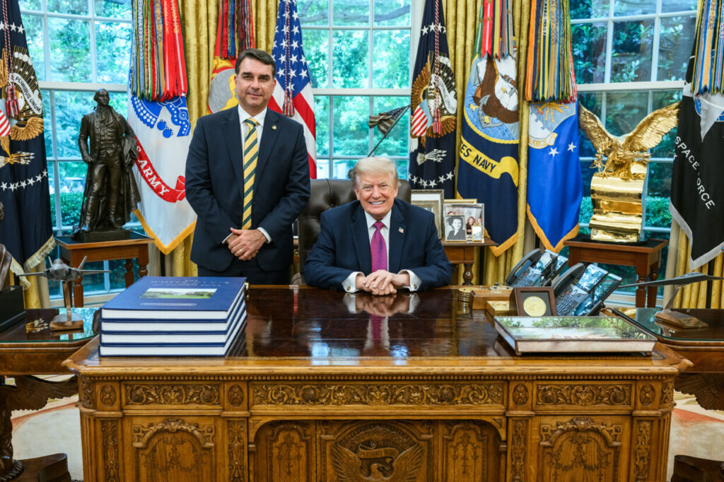 Flávio Bolsonaro stands beside US President Donald Trump at the Resolute Desk in the White House.