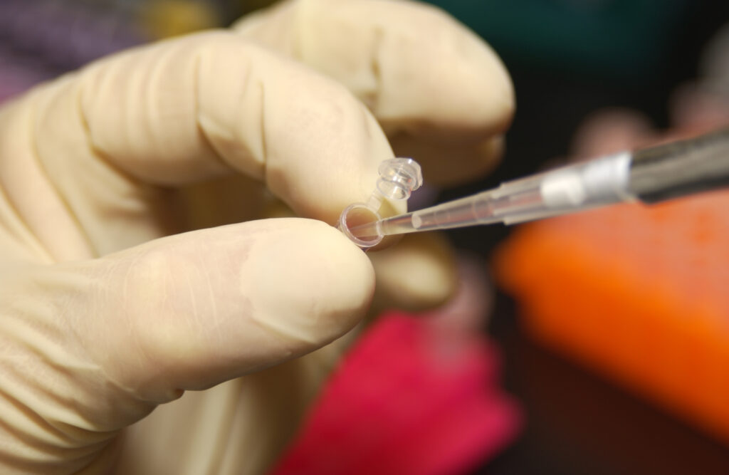 An NHGRI researcher uses a pipette to remove DNA from a micro test tube