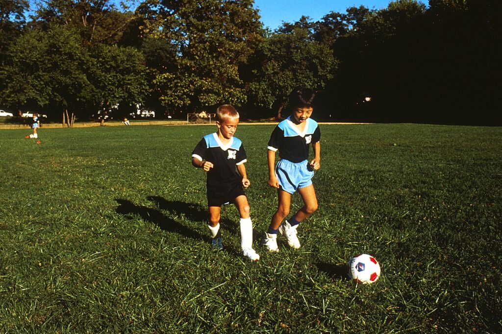 Two young children playing soccer with a ball on a grass field