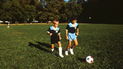 Two young children playing soccer with a ball on a grass field