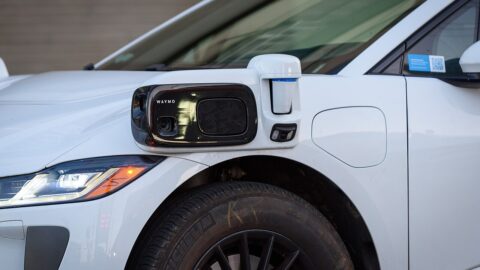 Close-up of a sensor package on the side of a white Waymo Jaguar I-PACE self-driving car, showing the camera and lidar units
