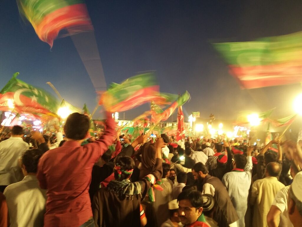 Supporters waving green-and-red PTI flags at a night rally in Pakistan