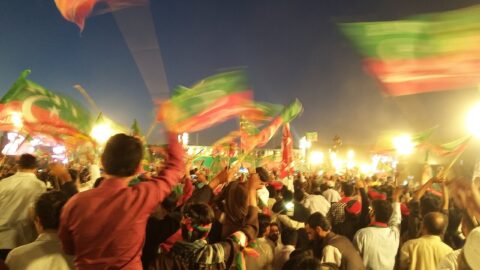 Supporters waving green-and-red PTI flags at a night rally in Pakistan