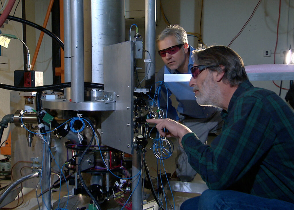Two NIST physicists standing beside the NIST-F2 cesium fountain atomic clock in a laboratory