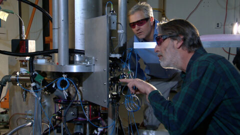 Two NIST physicists standing beside the NIST-F2 cesium fountain atomic clock in a laboratory