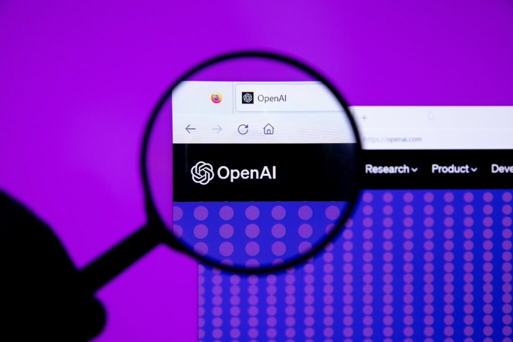 The OpenAI logo displayed on a computer screen, seen through a magnifying glass against a purple background