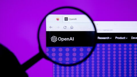 The OpenAI logo displayed on a computer screen, seen through a magnifying glass against a purple background