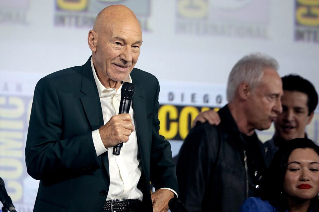 Patrick Stewart smiling with a microphone at a Star Trek panel, with Brent Spiner beside him.