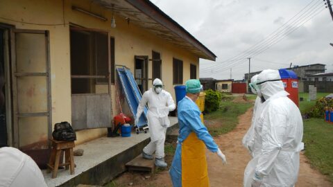 WHO health workers in protective gear outside an Ebola treatment unit.